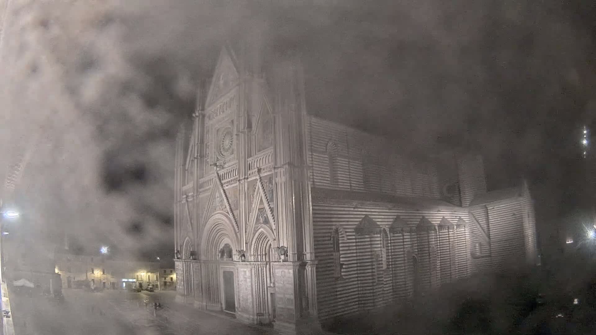 A large, striped stone cathedral is partially obscured by heavy fog at night.