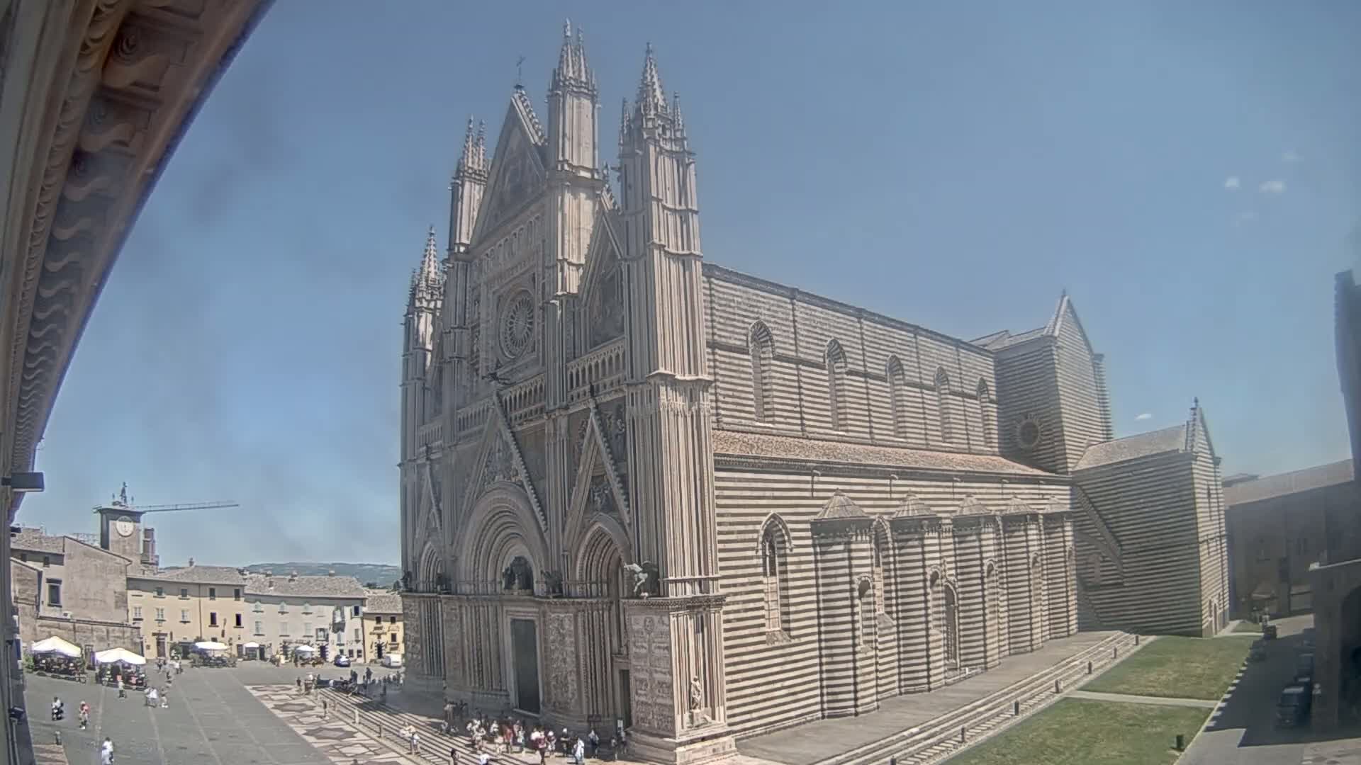 A large, striped stone cathedral stands in a town square on a sunny day.
