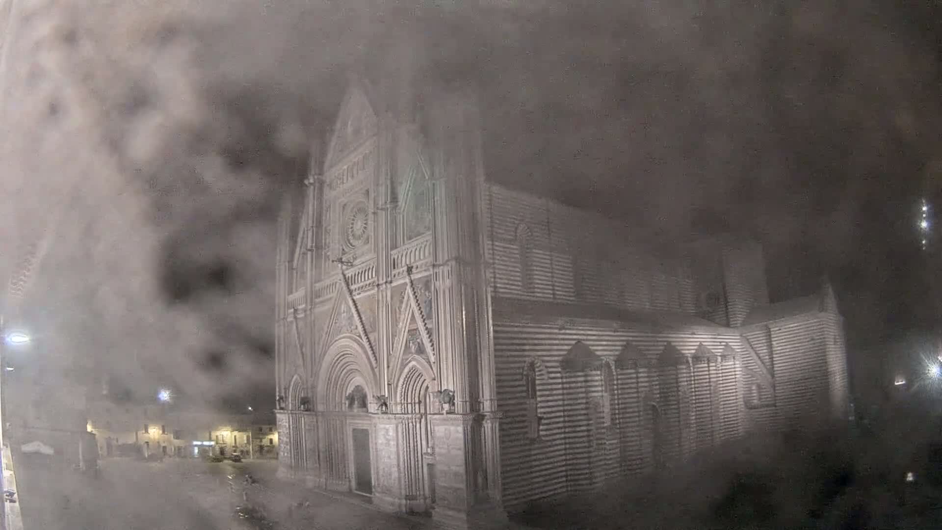 A large, striped stone cathedral is partially obscured by heavy fog at night.