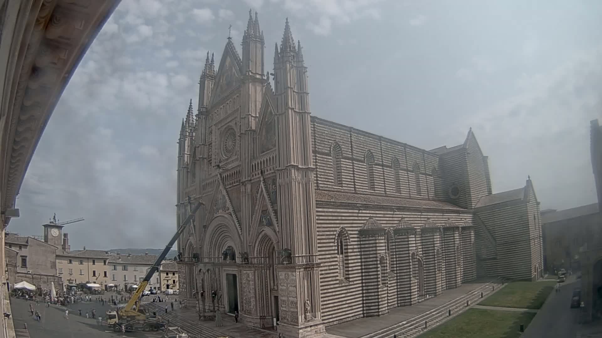 A large, striped cathedral stands under a partly cloudy sky, with a crane and people visible in the foreground.