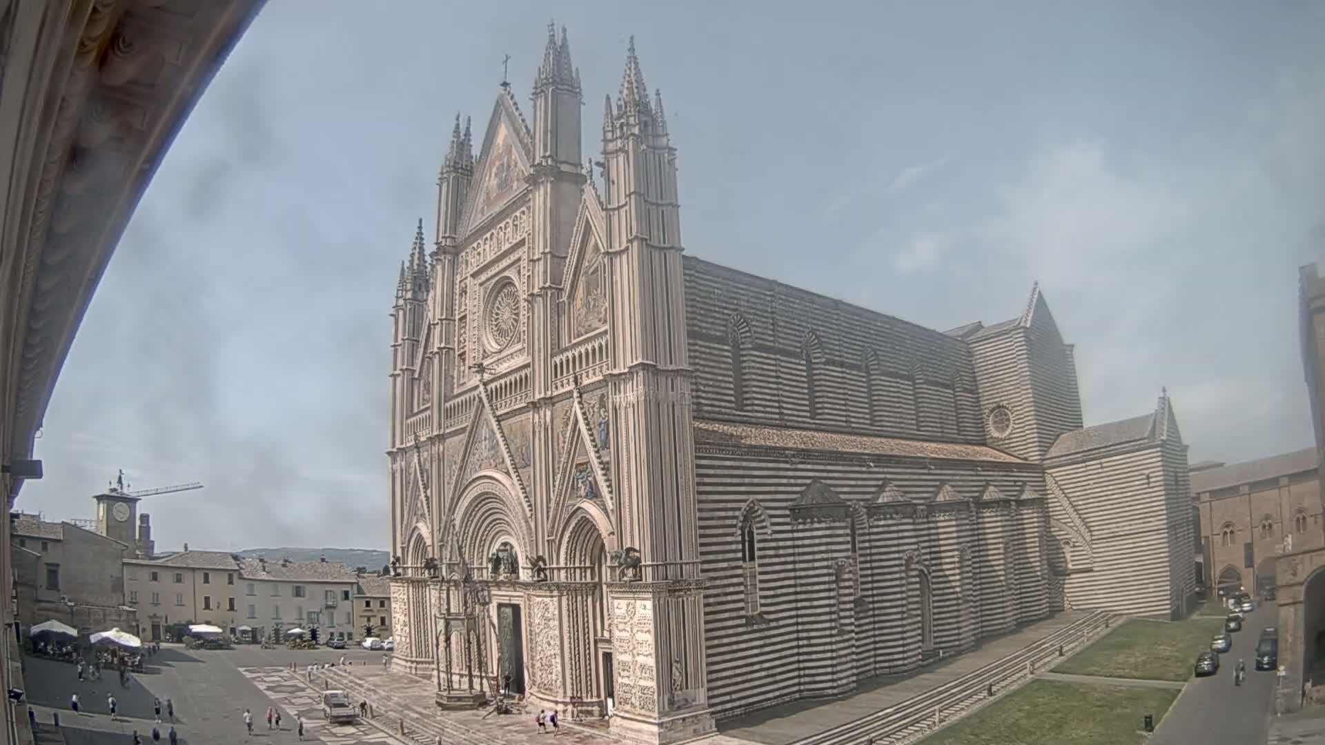 A large, striped cathedral stands in a town square on a partly cloudy day.