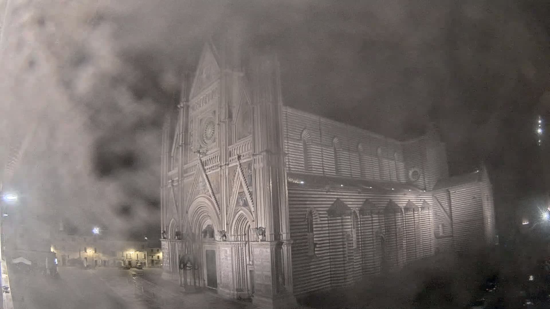 A large, striped stone cathedral is seen at night in foggy conditions.