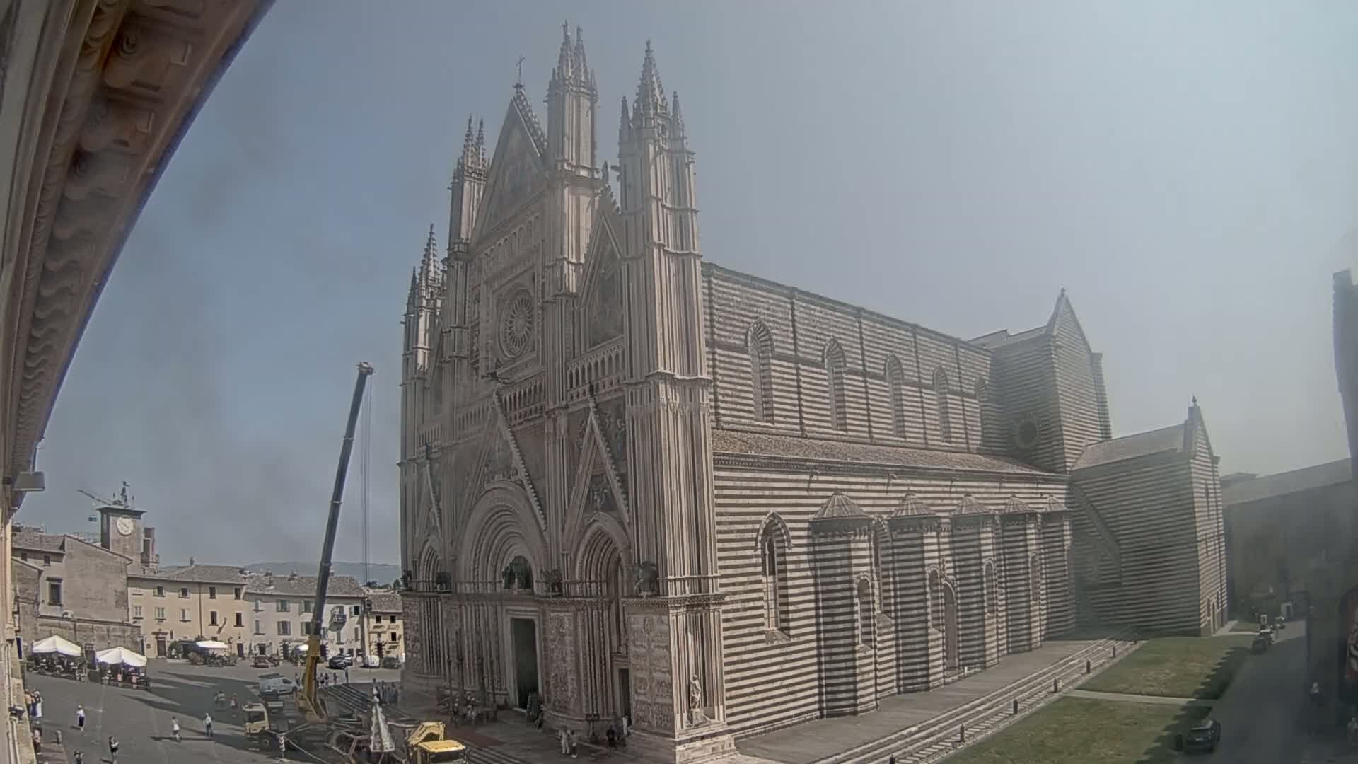 A large, striped cathedral with Gothic architectural features is partially obscured by a construction crane on a sunny day.