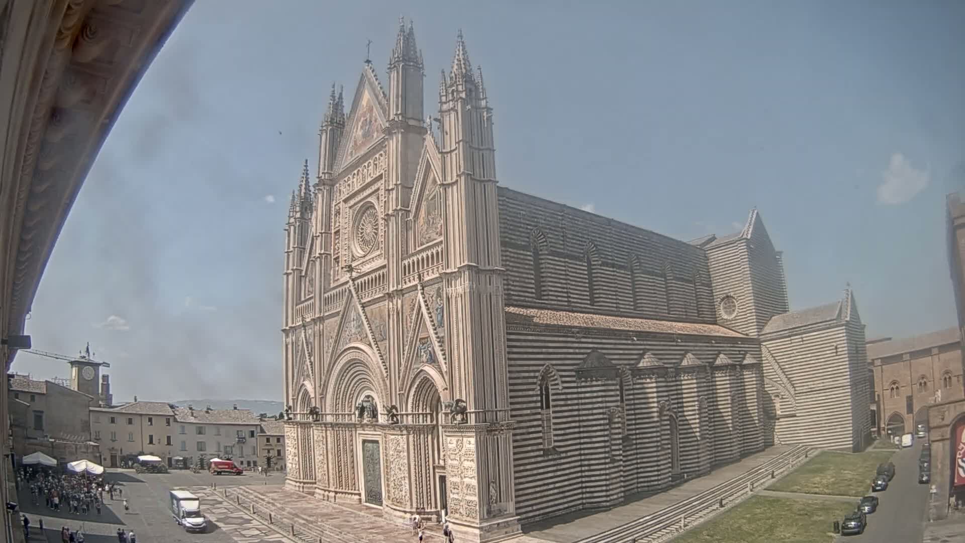 A large, ornate cathedral with striped exterior walls stands in a town square on a sunny day.