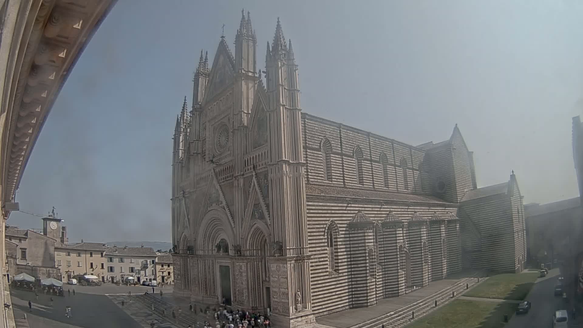 A large, striped cathedral stands in a town square on a hazy, sunny day.
