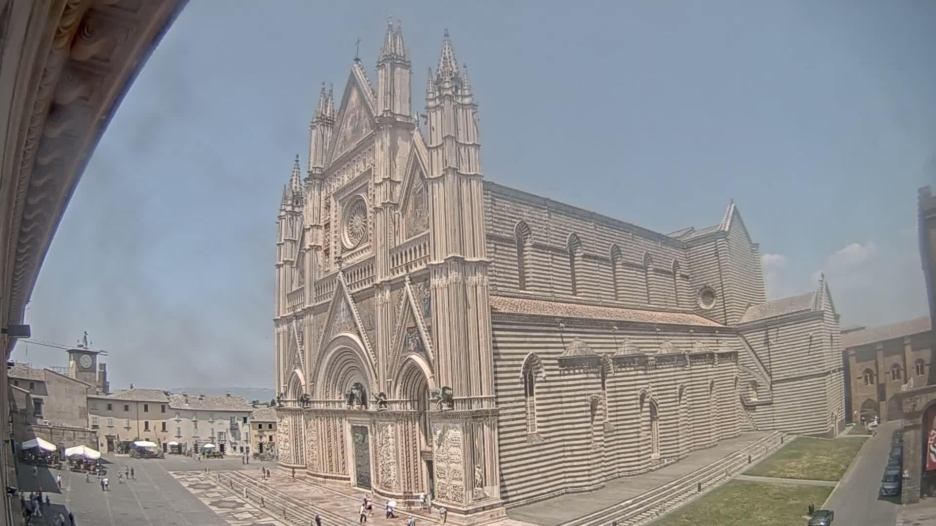 A large, striped stone cathedral stands in a town square on a sunny day.