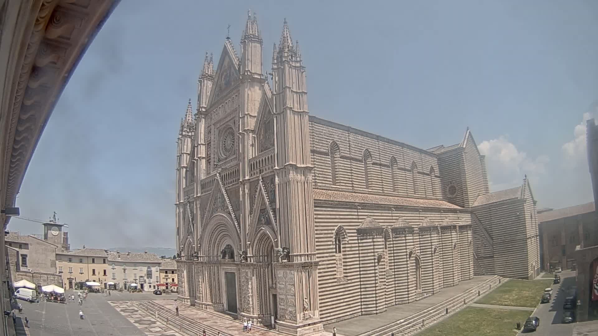 A large, striped stone cathedral stands in a town square on a sunny day.
