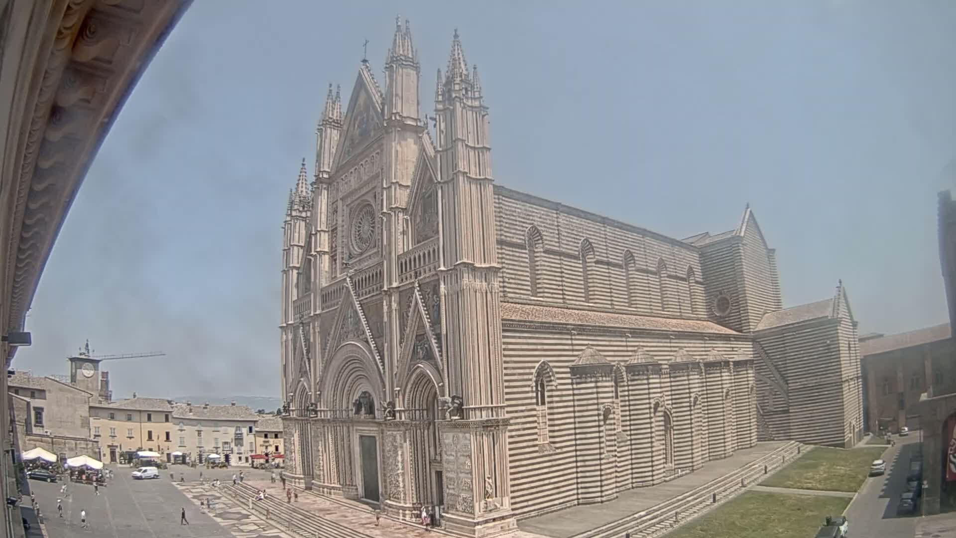 A large, striped stone cathedral stands in a town square on a sunny day.