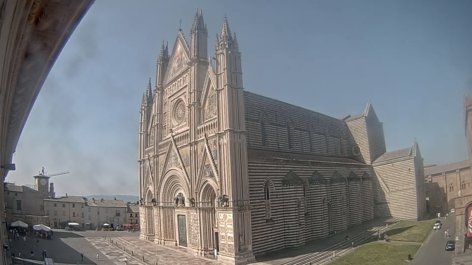 A large, striped cathedral stands in a town square on a sunny day.