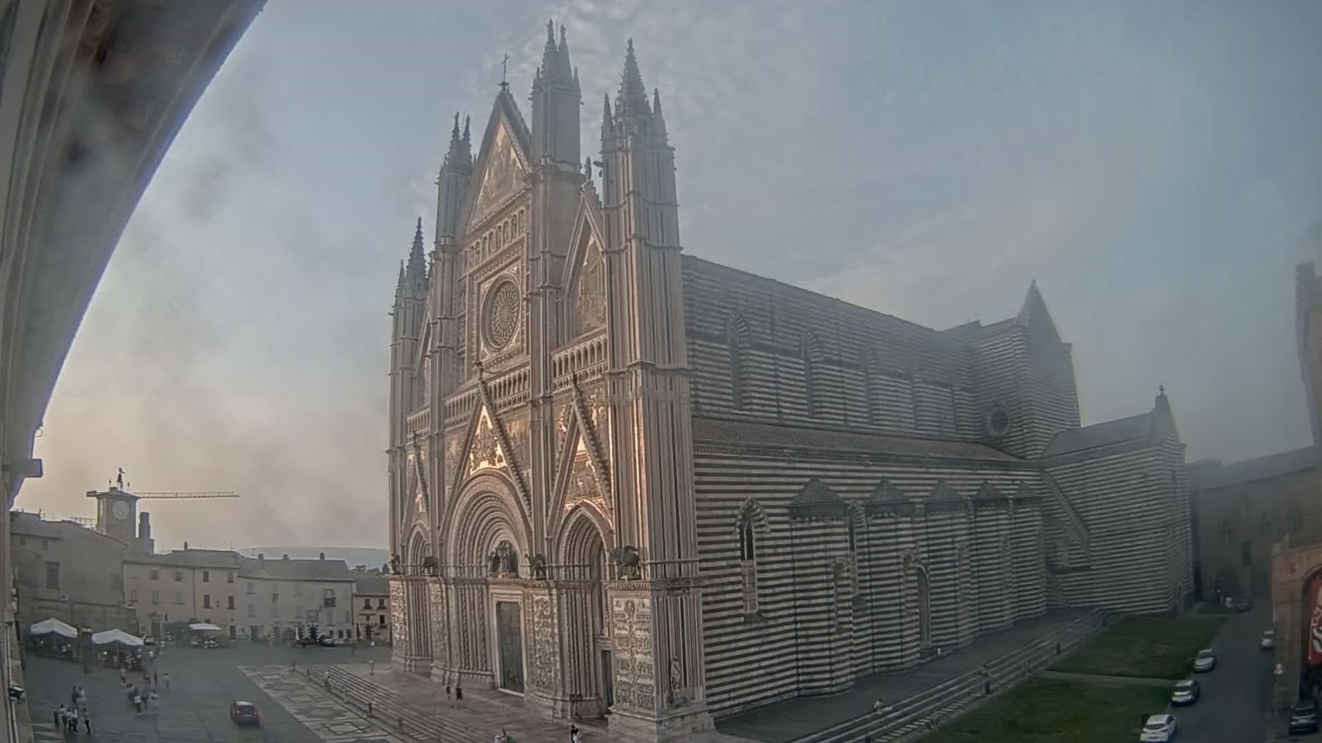 A large, striped cathedral stands in a town square on a hazy day.