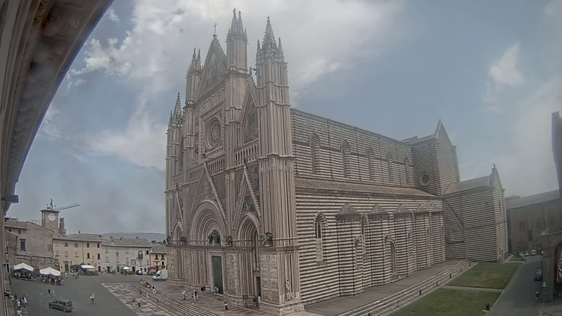 A large, striped stone cathedral stands in a town square on a partly cloudy day.