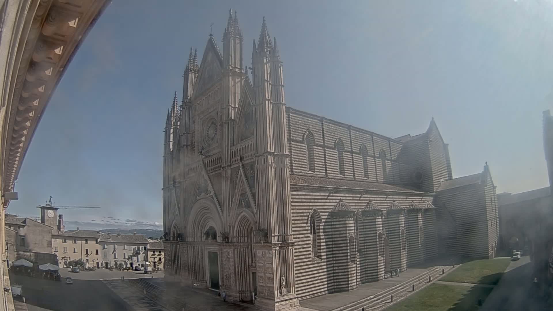 A large, striped cathedral stands in a town square on a sunny day.