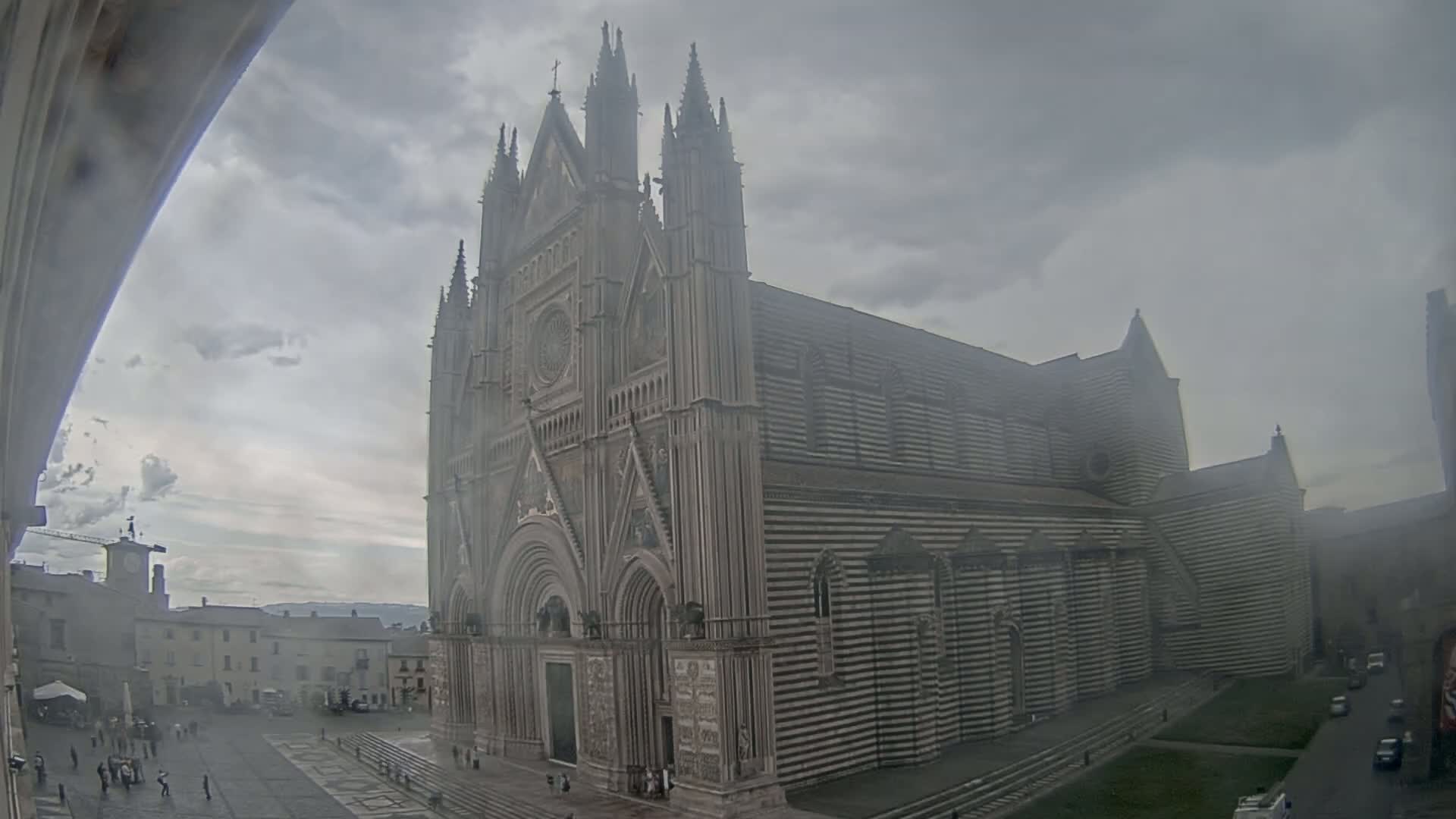 A large striped cathedral stands in a town square on an overcast day.