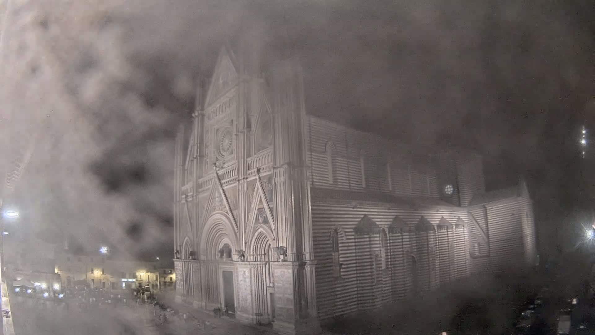 A large, striped stone cathedral is partially obscured by heavy fog at night.
