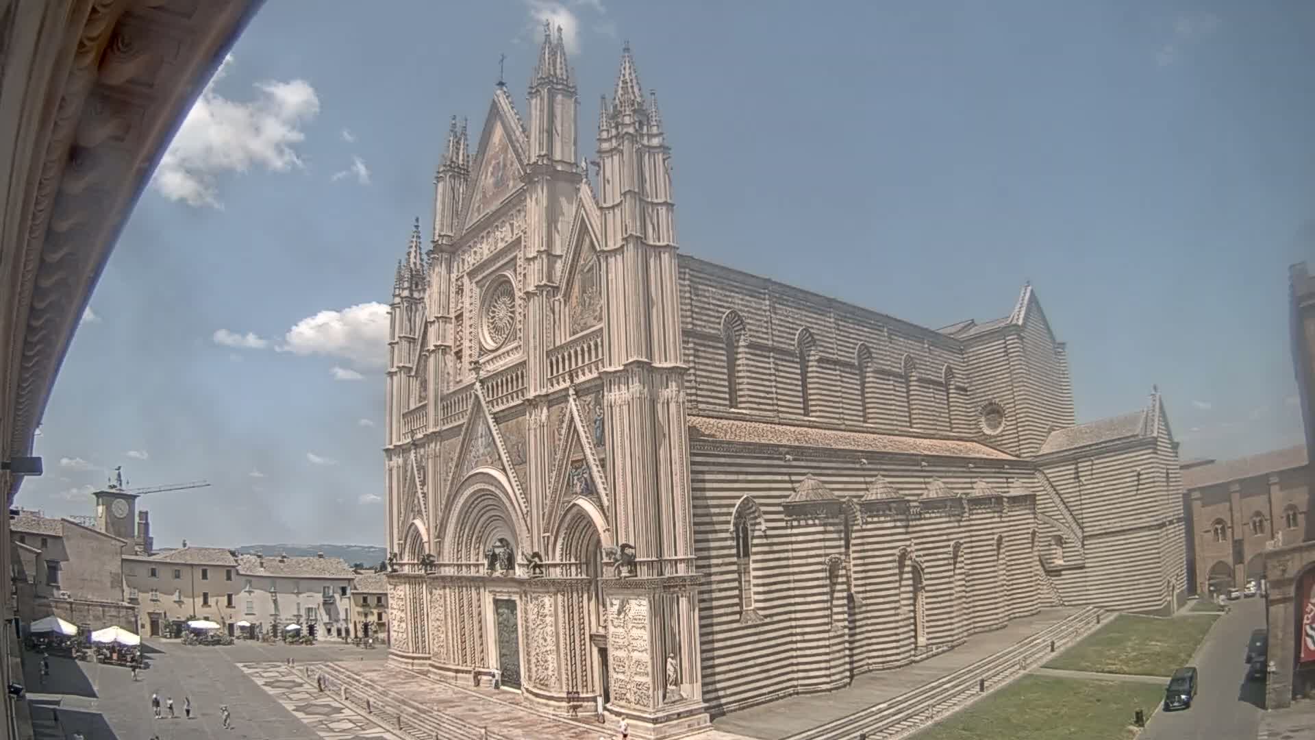 A large, ornate cathedral with striped exterior walls stands in a town square on a partly cloudy day.