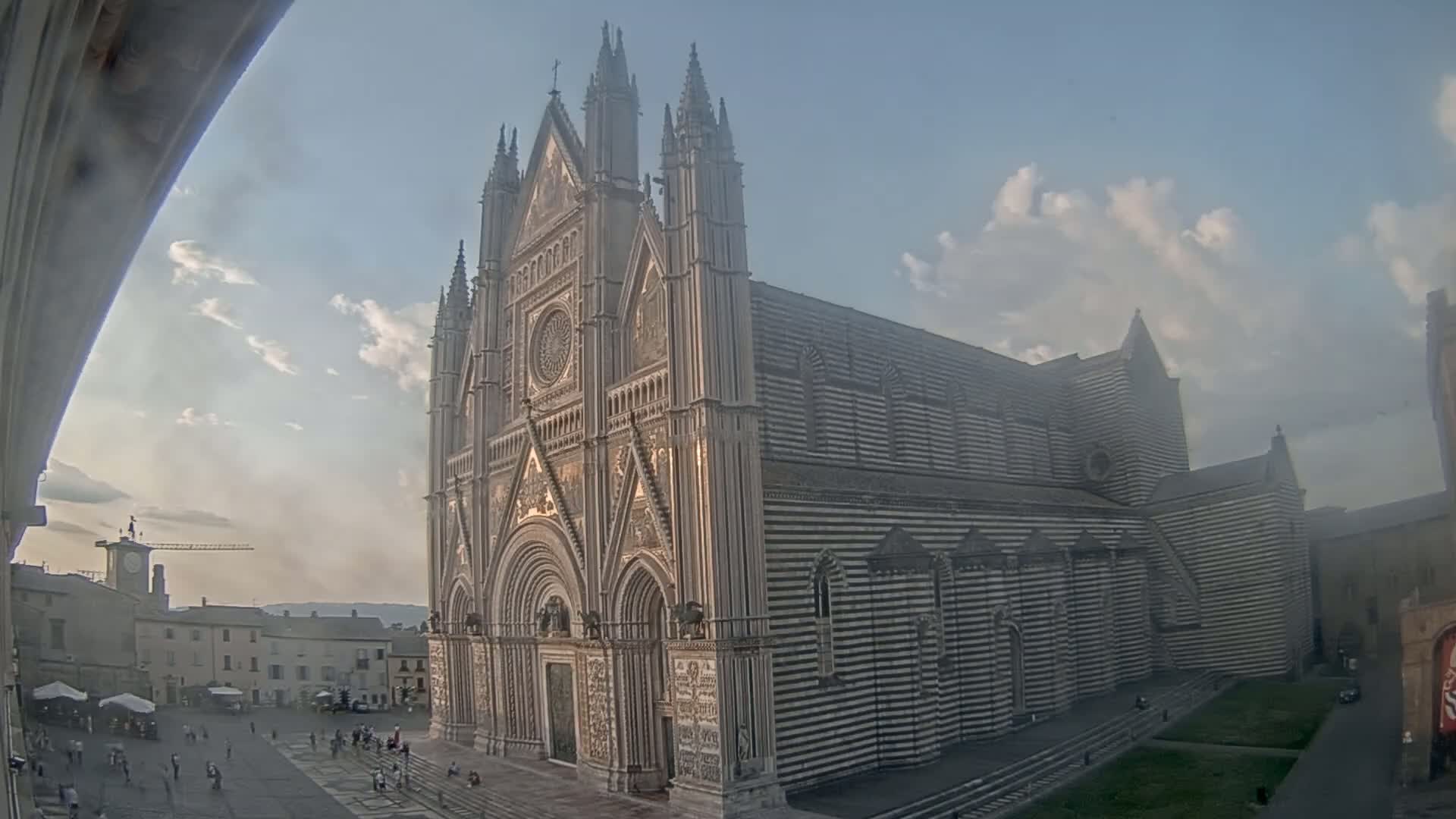 A large, striped cathedral stands in a town square on a partly cloudy day.