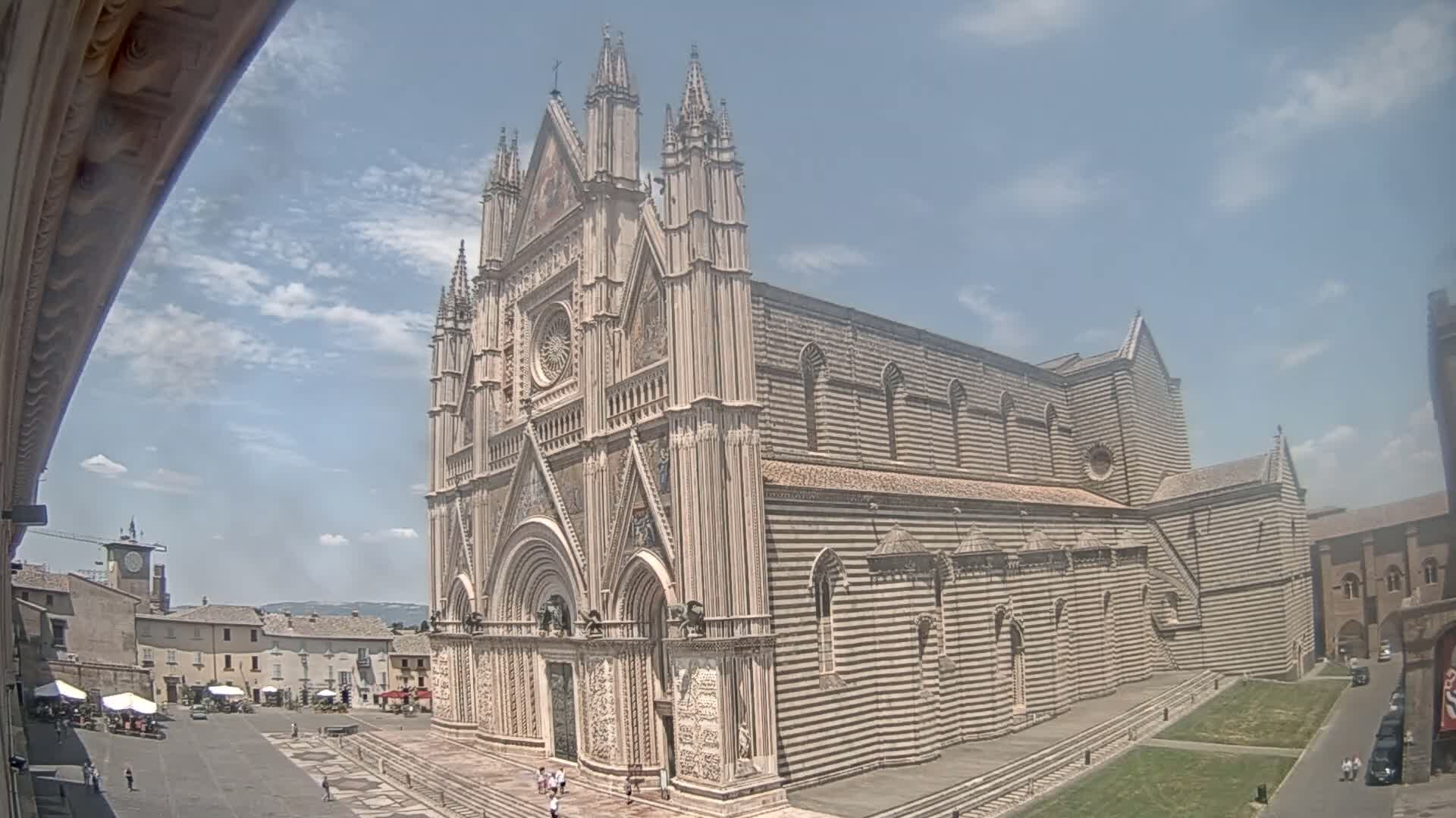 A large, striped stone cathedral stands in a town square on a partly sunny day.