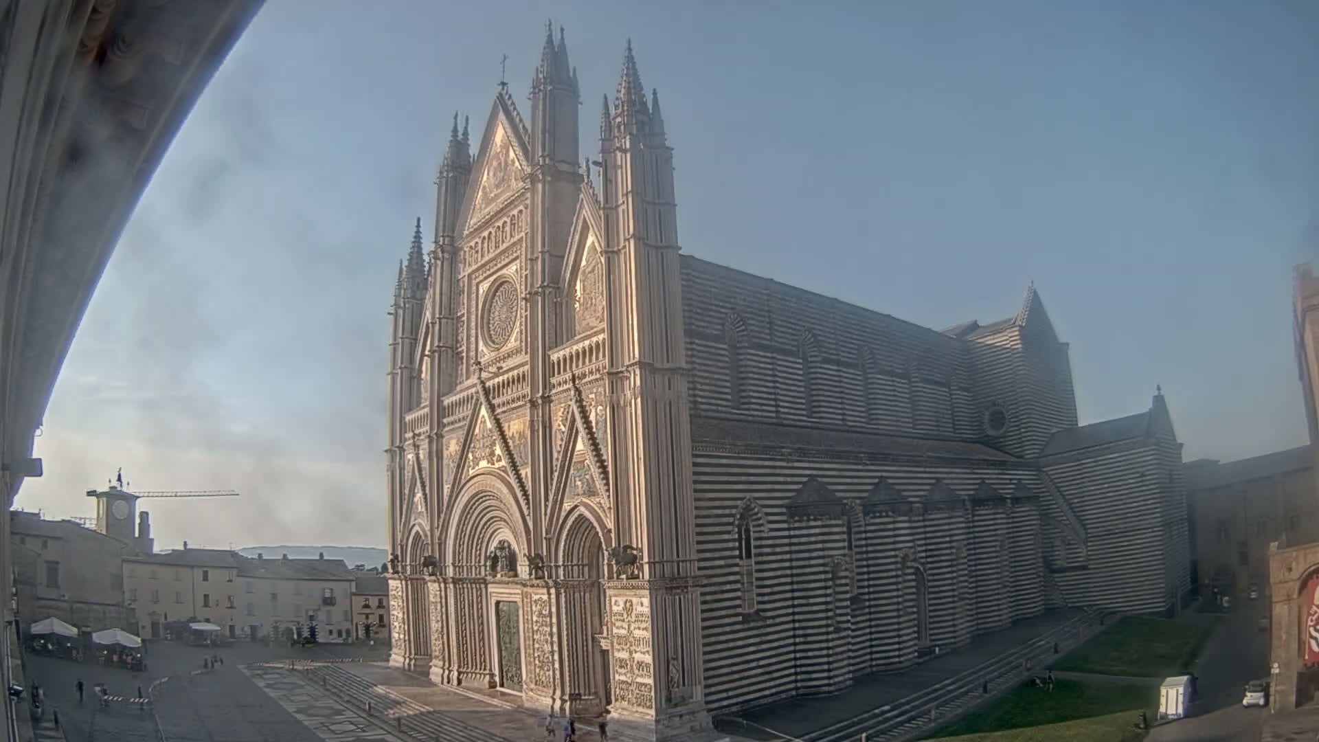 A large, striped cathedral stands in a town square on a mostly clear day.
