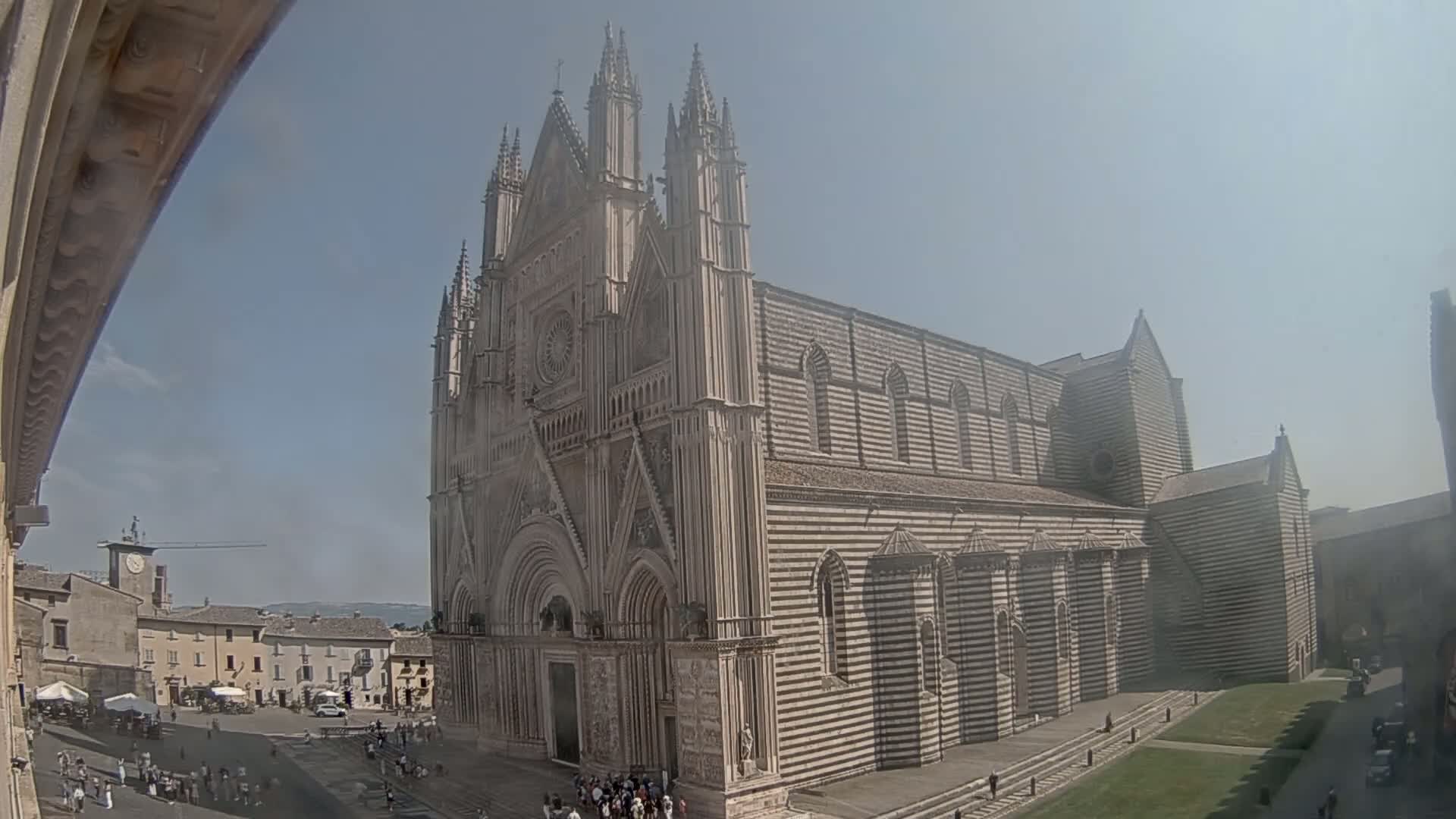 A large, striped stone cathedral stands in a town square on a sunny day.