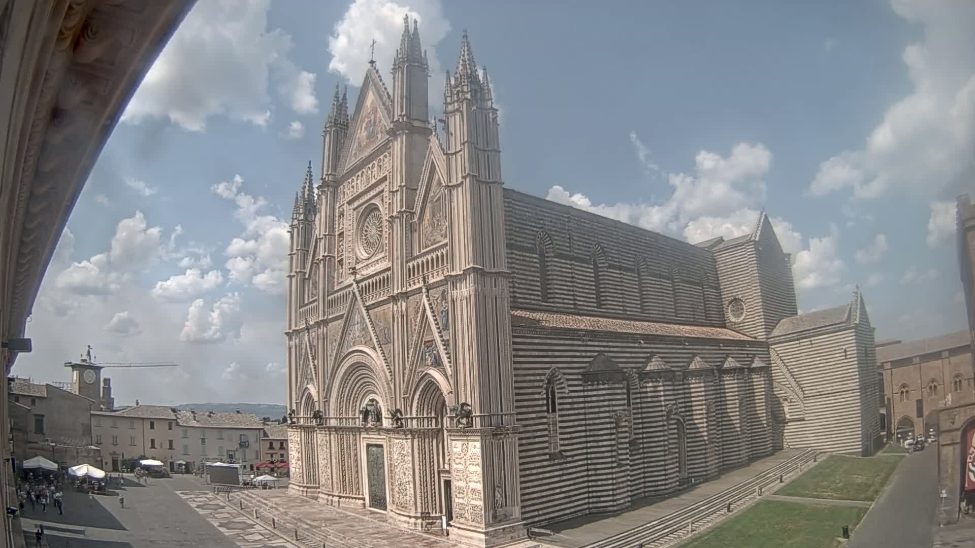 A large, striped cathedral stands in a town square under a partly cloudy sky.