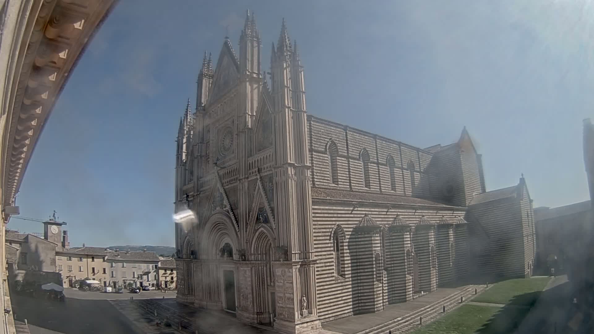 A large, striped stone cathedral stands in a town square on a sunny day.