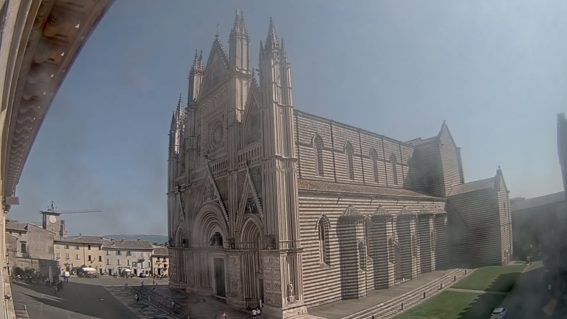 A large striped stone cathedral stands in a town square on a sunny day.