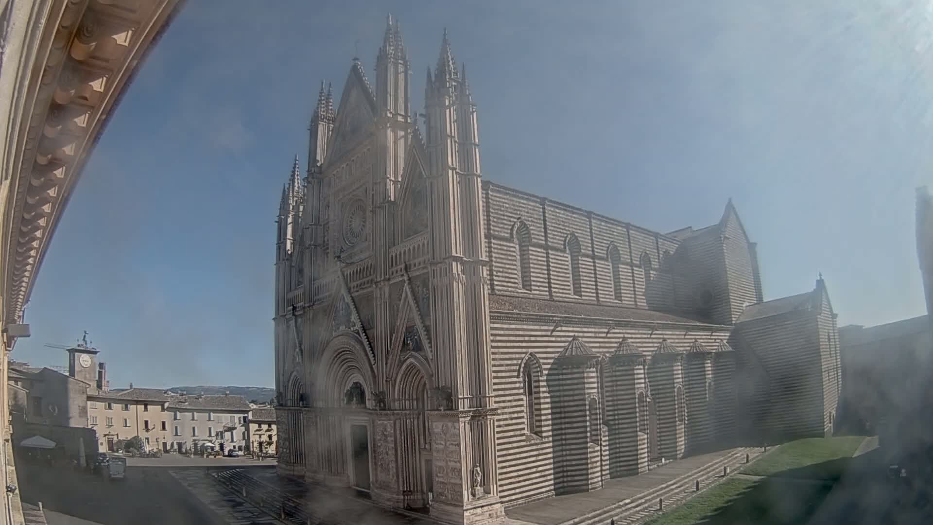 A large, striped stone cathedral stands in a town square on a hazy, sunny day.