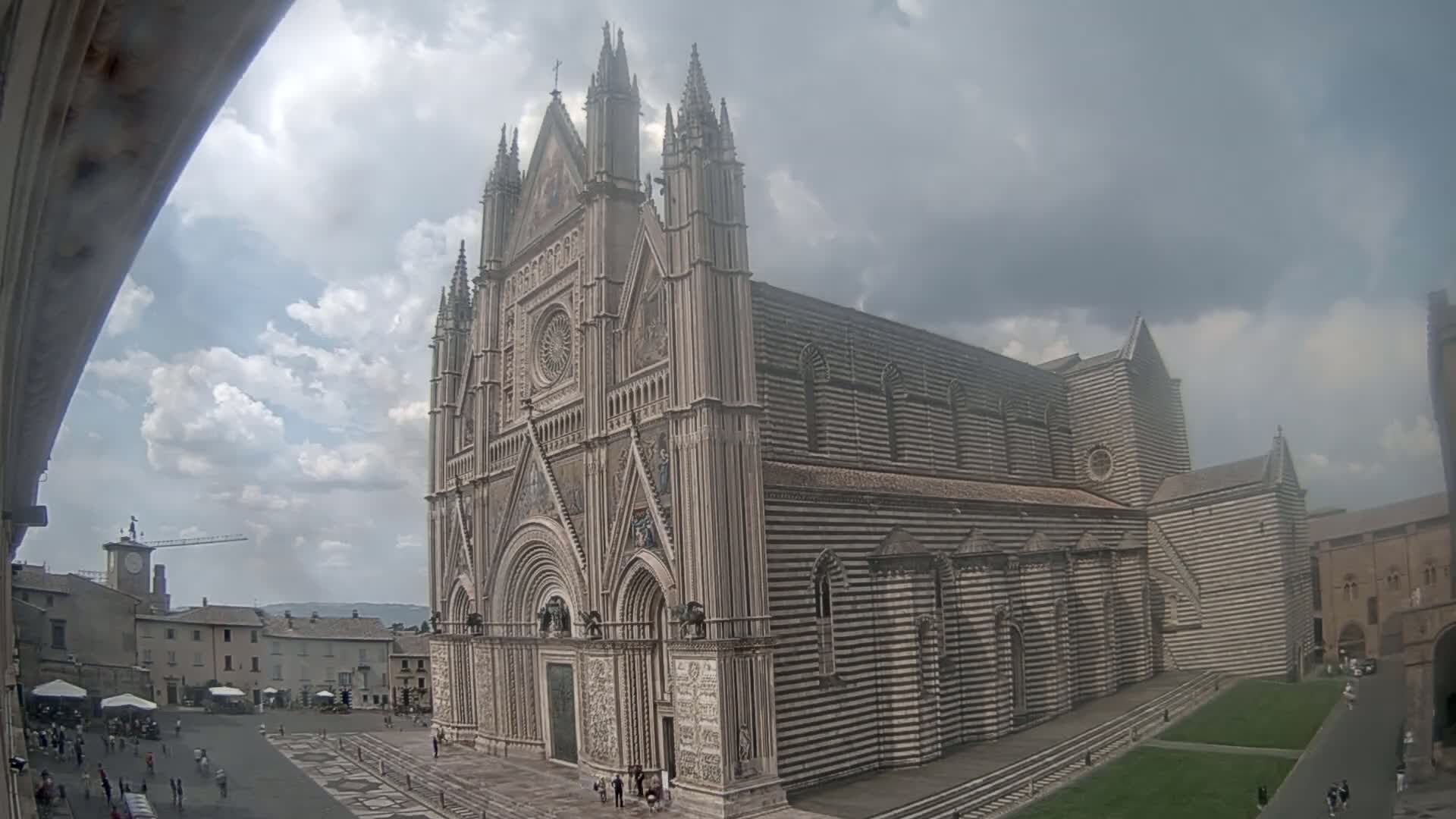 A large, striped, Gothic-style cathedral stands in a town square under a partly cloudy sky.