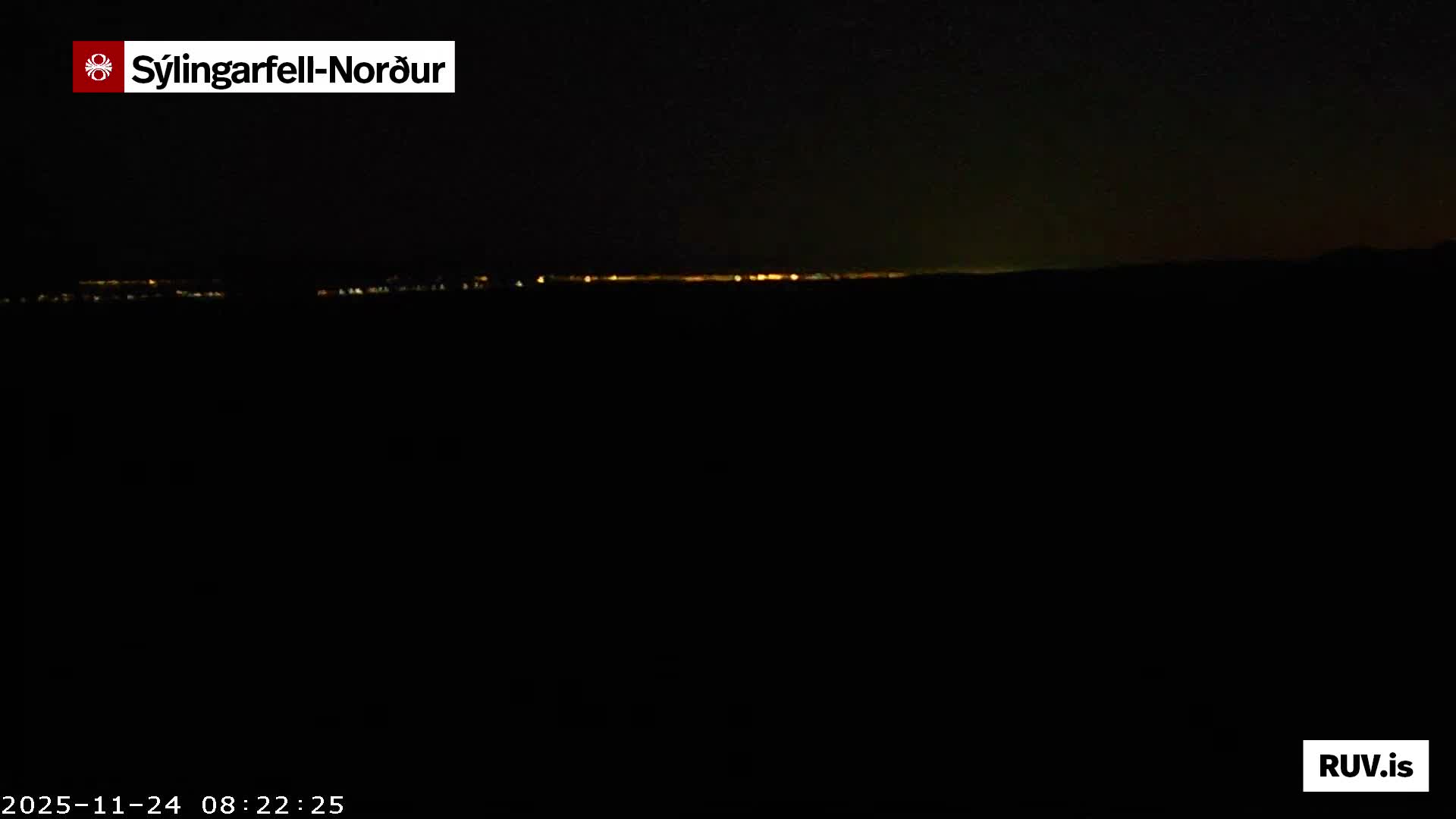 A very dark night scene displays a faint, distant horizontal line of lights along the horizon under clear conditions.
