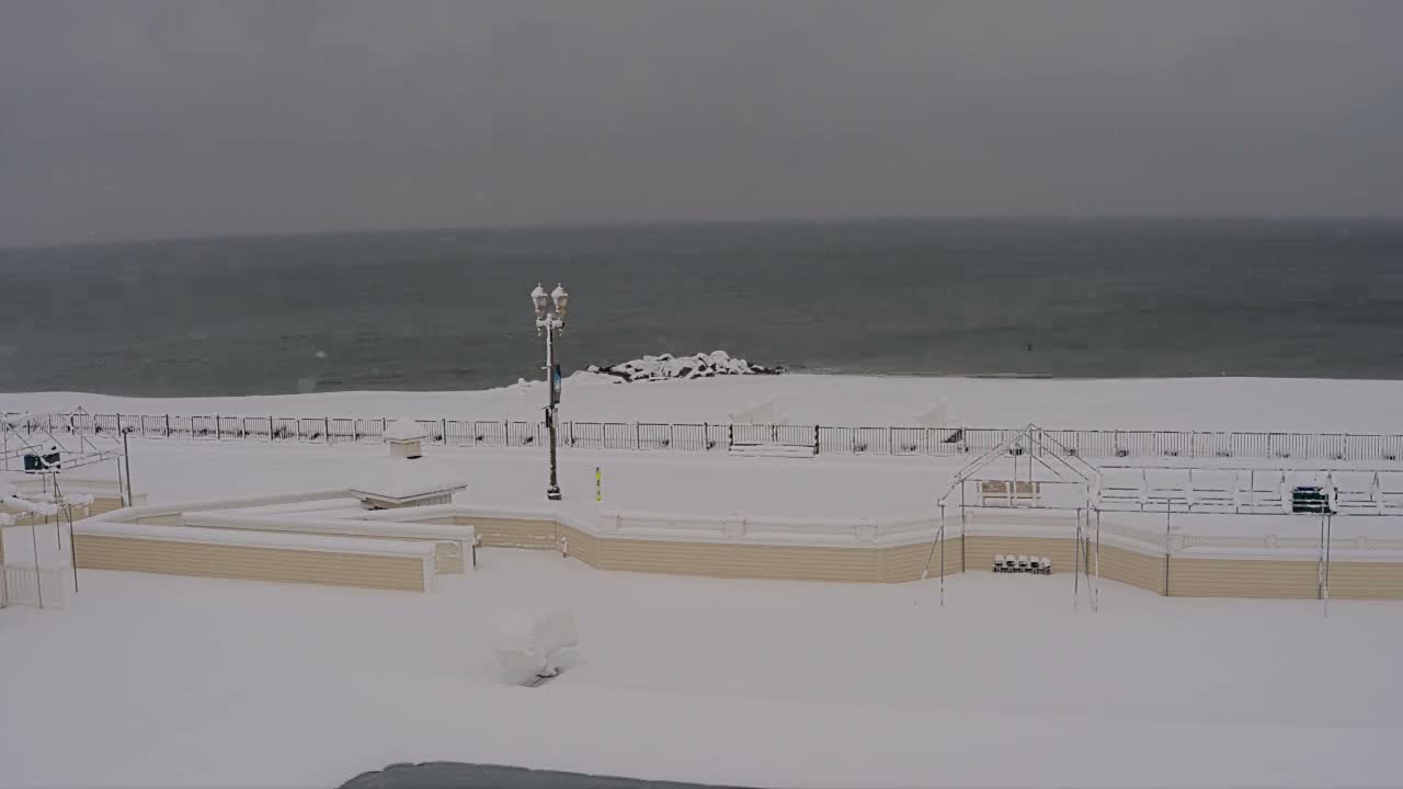 A tranquil nighttime scene displays a partially lit boardwalk and sandy beach alongside a dark ocean with visible waves, all under a clear night sky.