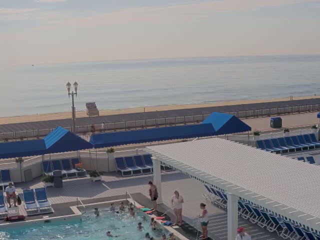 A nighttime view of a closed pool area with blue lounge chairs and umbrellas near an ocean under a dark sky.