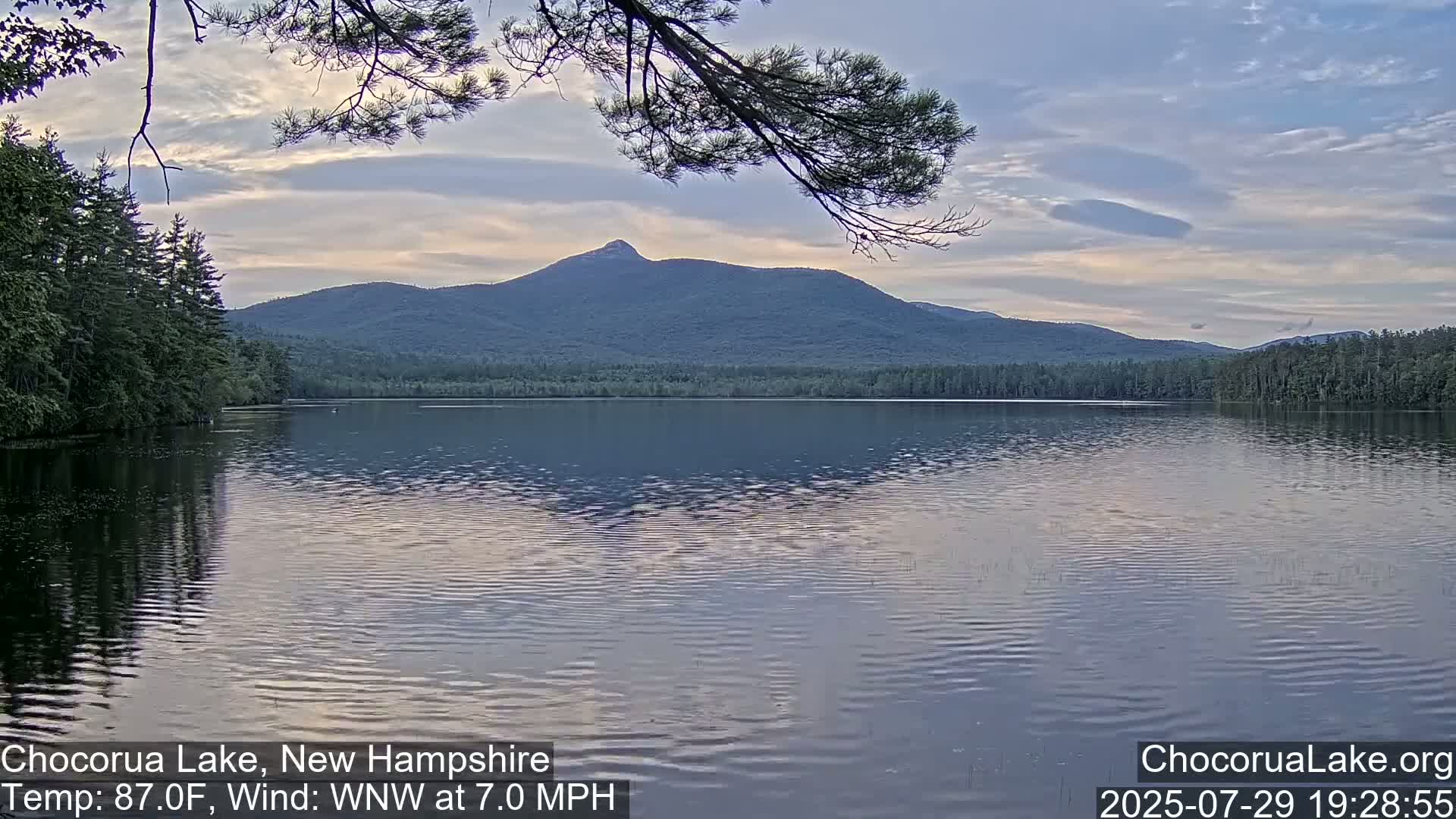 A dark, still lake is seen at dusk, with a mountain silhouetted in the distance under a clear sky.
