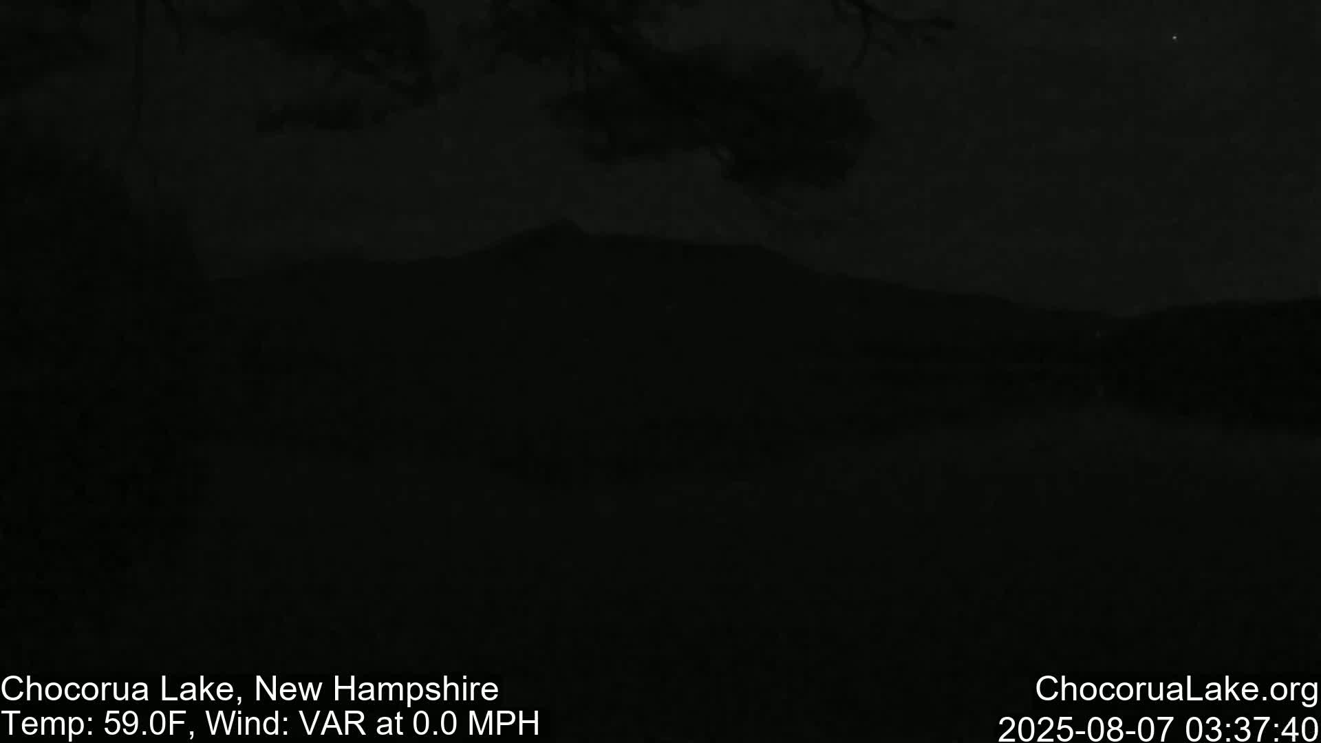 A dark, nighttime scene shows a silhouetted mountain range against a cloudy sky.