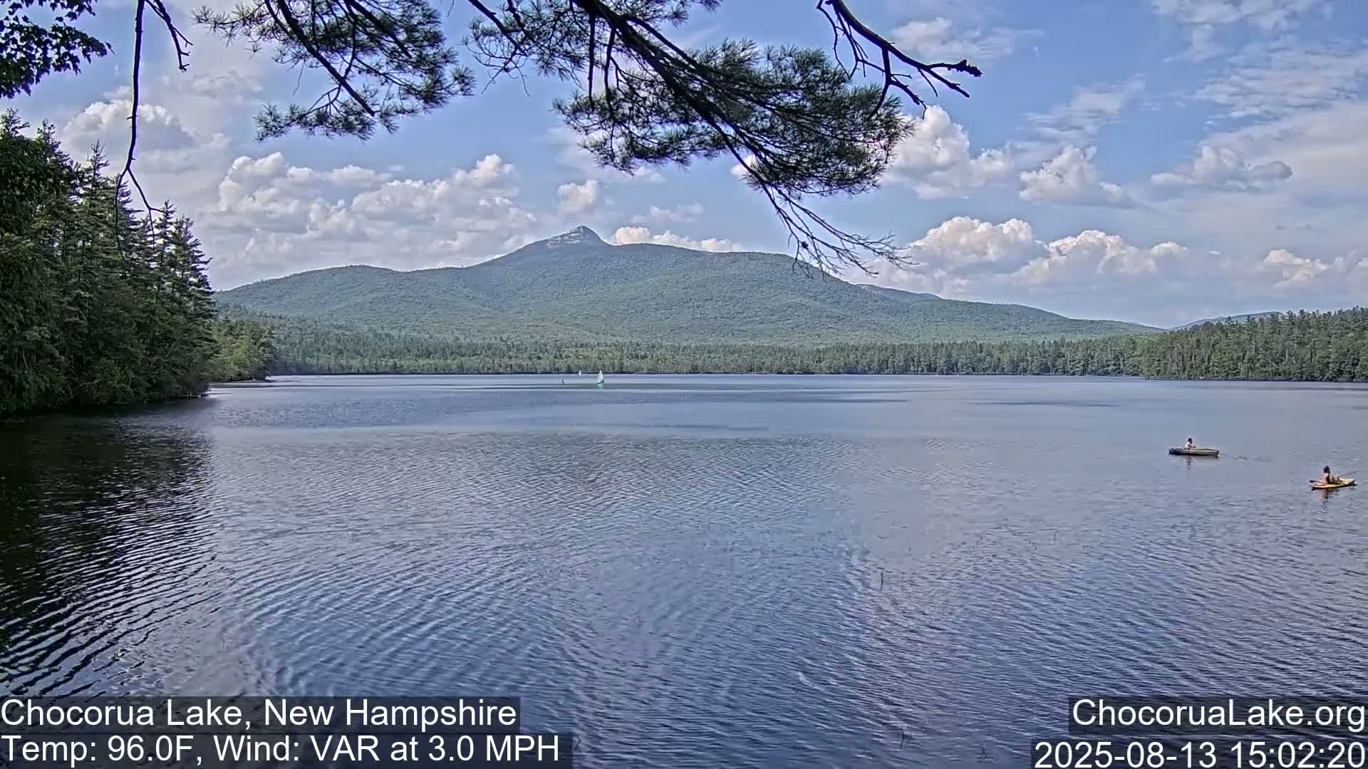 A calm lake with two small boats and a mountain in the background under a partly cloudy sky.