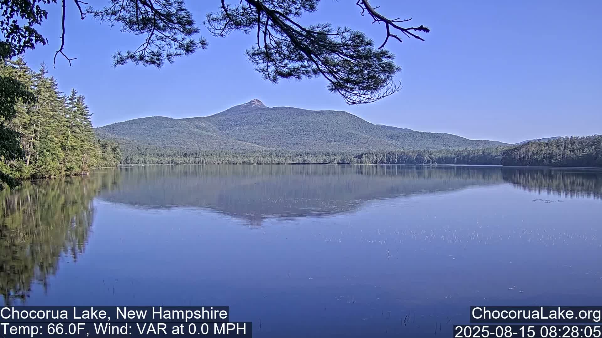 A calm lake with two small boats and a mountain in the background under a partly cloudy sky.