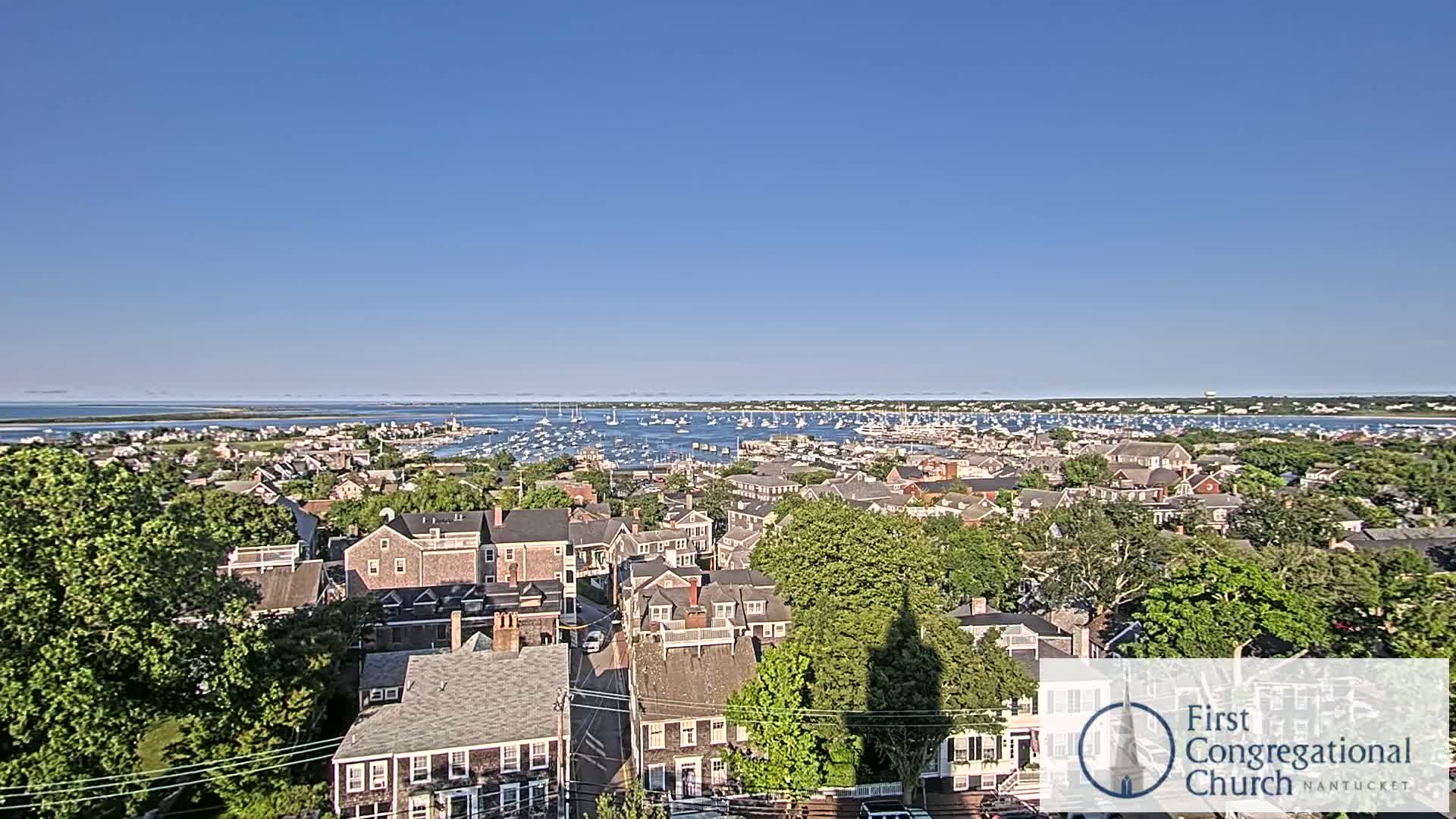An elevated view of a coastal town on an overcast day shows a harbor filled with boats in the distance.