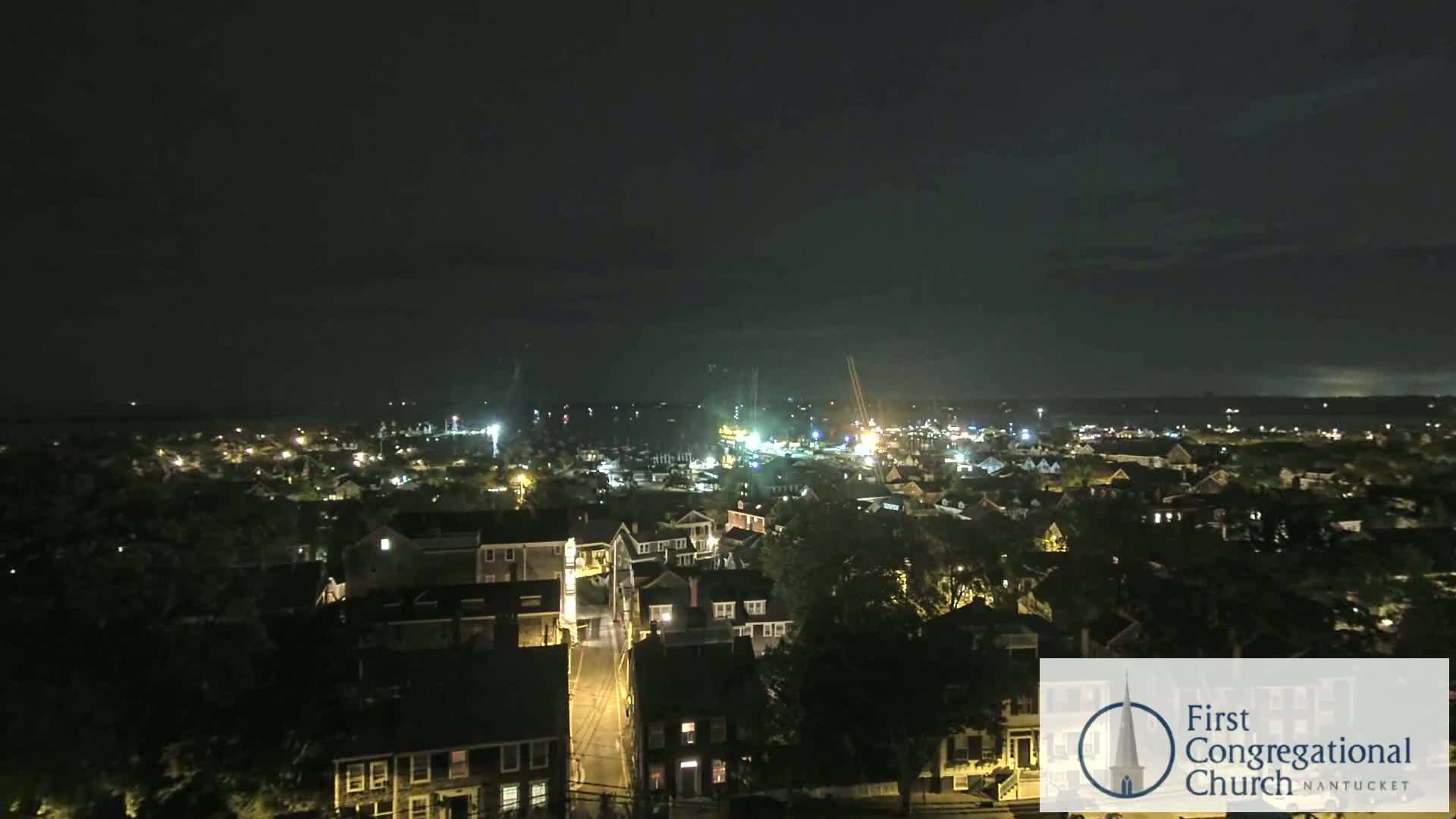 A nighttime aerial view of a town with houses and streets illuminated, under a dark, clear sky.
