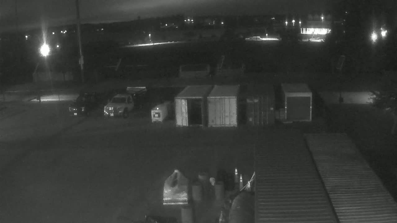 At night, several vehicles and shipping containers are parked in a dimly lit, outdoor lot.