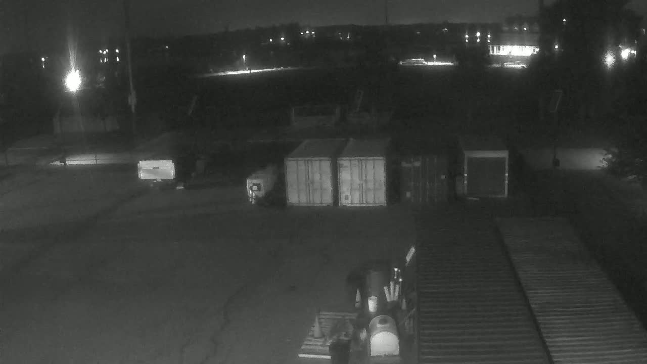 At night, a forklift is near several shipping containers in a dark, paved outdoor area.