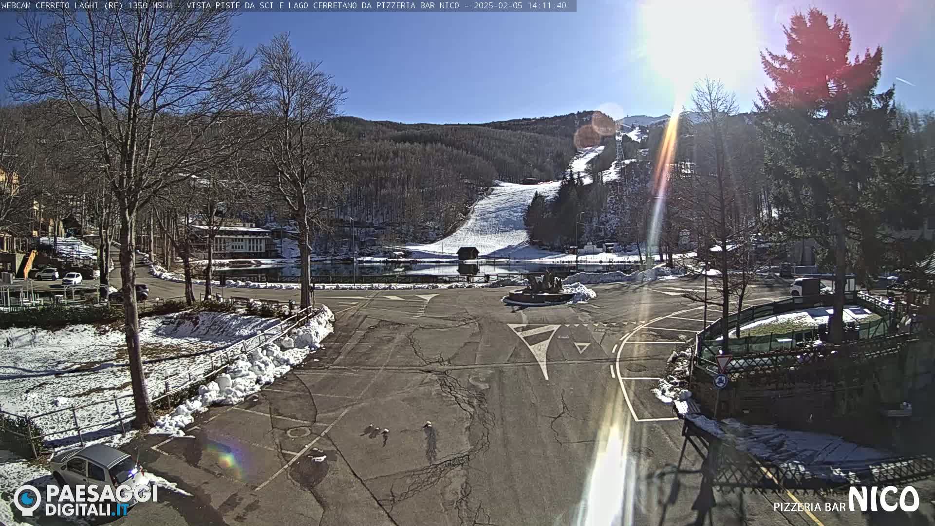 A sunny day reveals a parking lot and surrounding buildings near a snow-covered ski slope and lake.