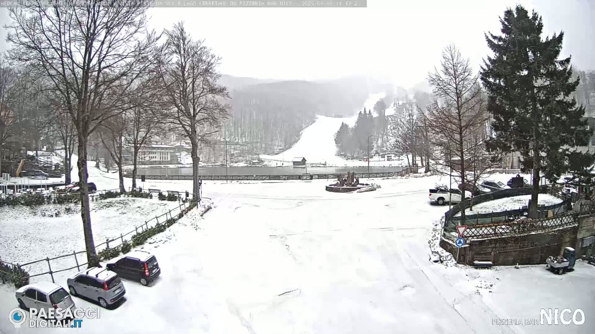 A snow-covered parking lot and plaza, with a ski slope visible in the background under a heavy, overcast sky.