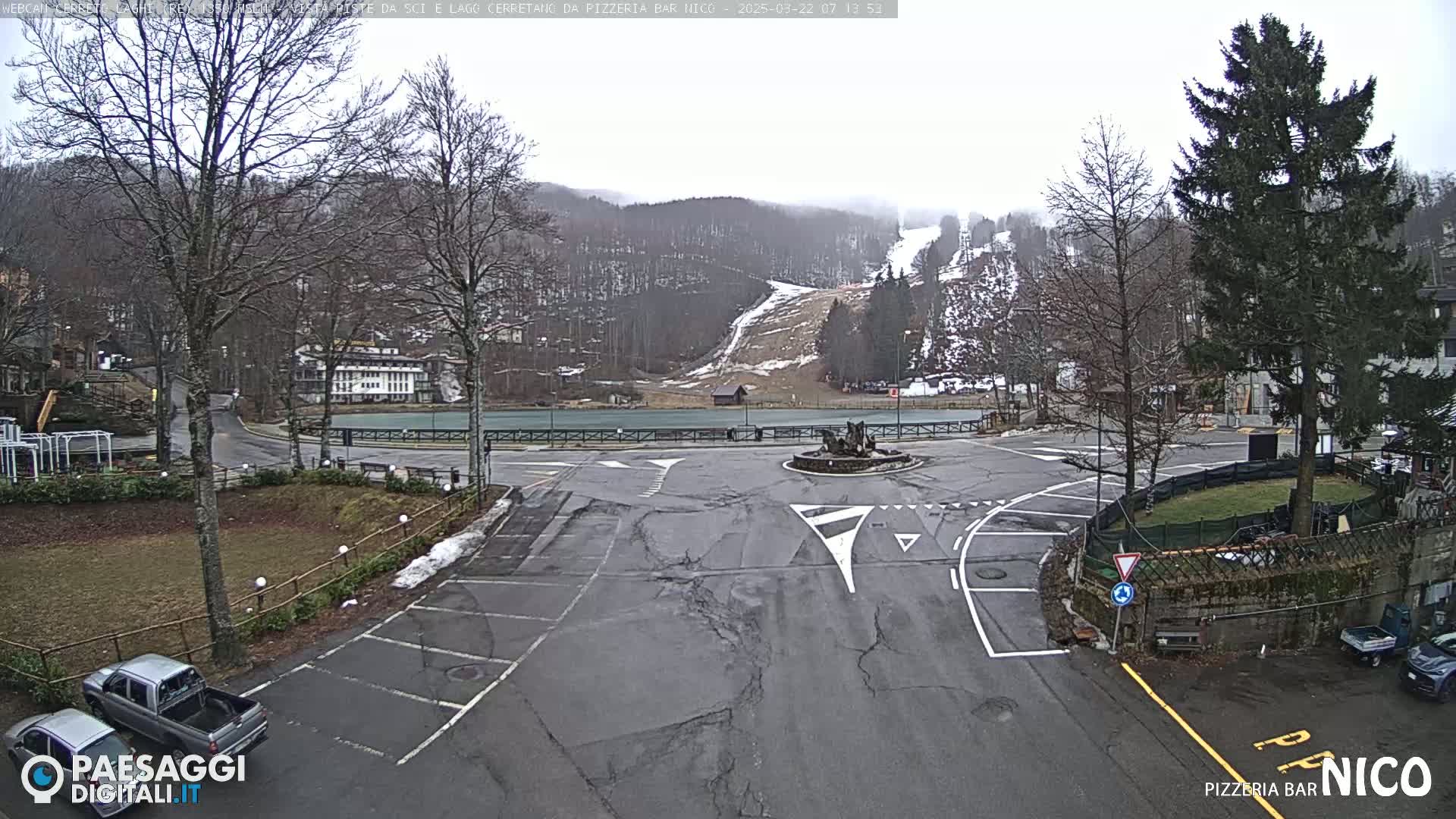 A mostly empty parking lot and roundabout are situated in front of a ski slope on an overcast day.