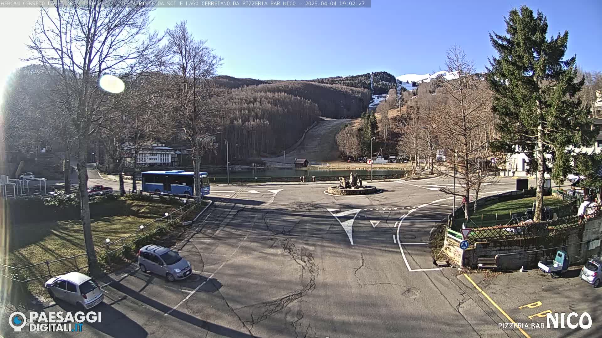 A sunny day reveals a parking lot and roundabout in a mountain town, with a ski slope visible in the background.