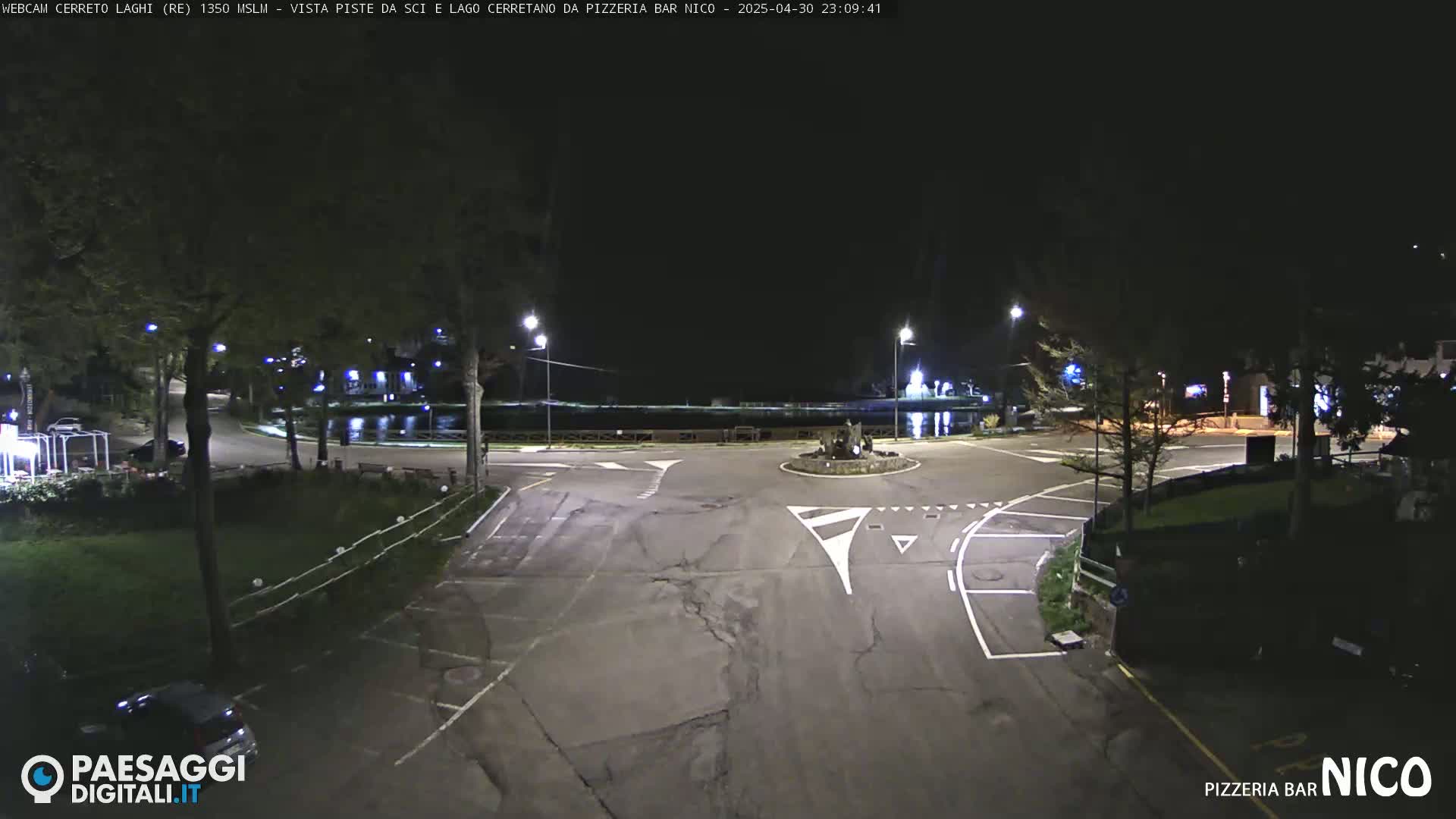 A nighttime view of a paved intersection near a body of water, illuminated by streetlights.