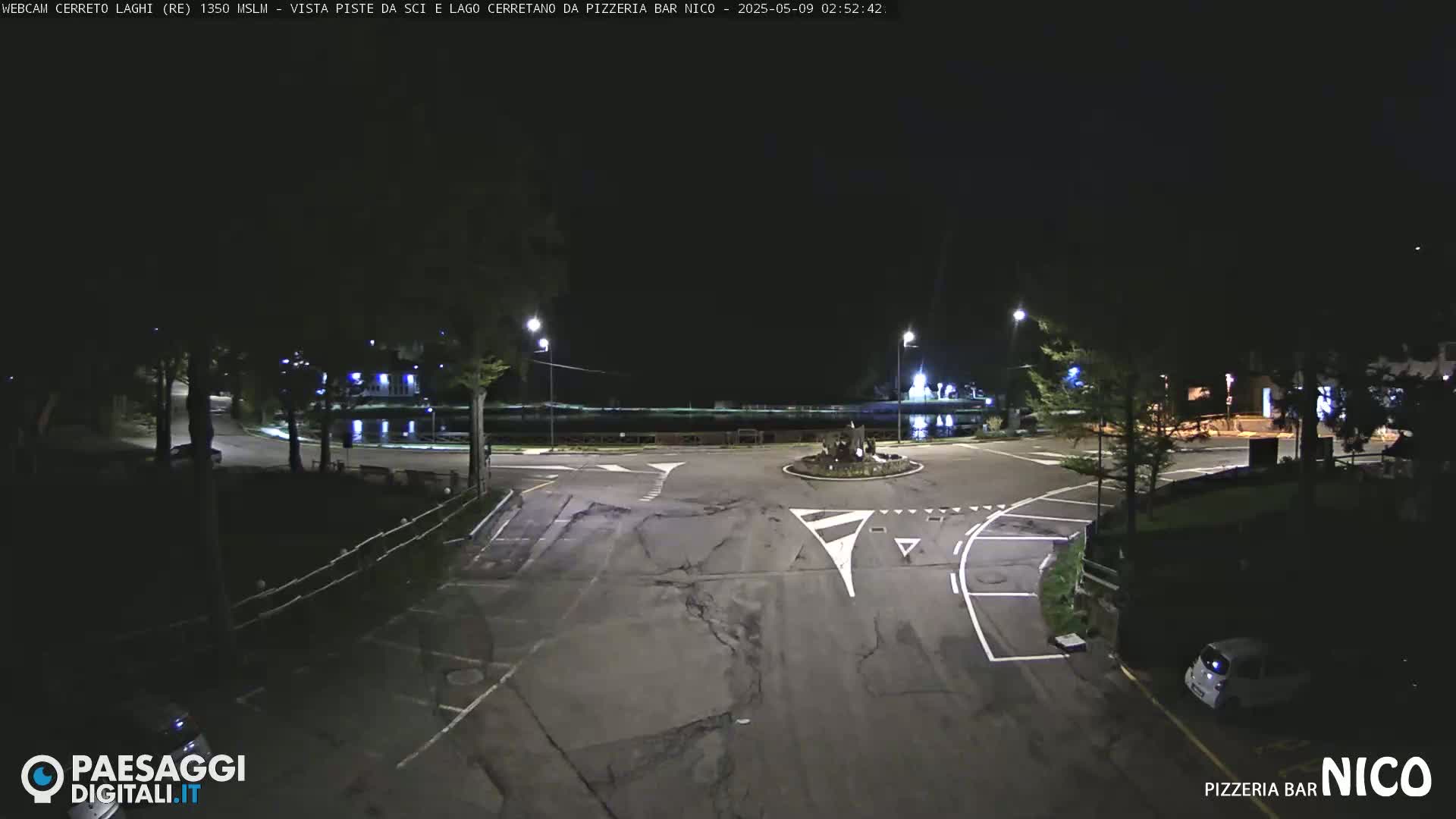 A nighttime view of a roundabout and parking lot near a body of water, illuminated by streetlights.