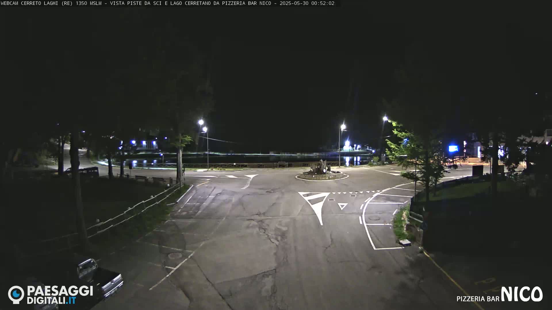 A nighttime view of a mostly empty parking lot and roundabout near a body of water, illuminated by streetlights.