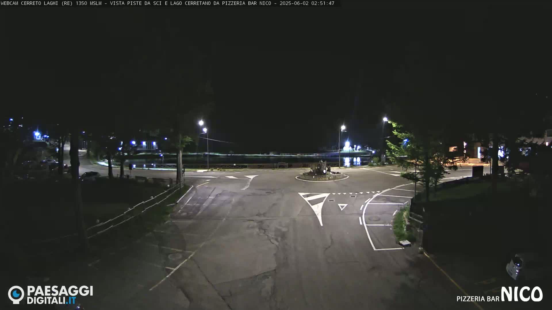 A nighttime, dimly lit view of a mostly empty roundabout and surrounding roadway.
