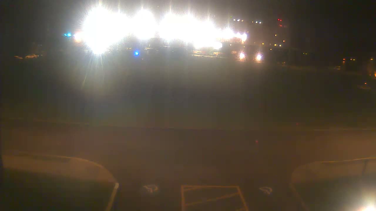 A nighttime outdoor scene displays an array of bright, blooming lights in the distance, illuminating a large dark ground area with faint markings in the foreground.