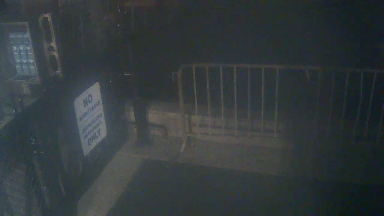 A dimly lit, dark area shows a metal barricade and a person standing near a "no admittance" sign.