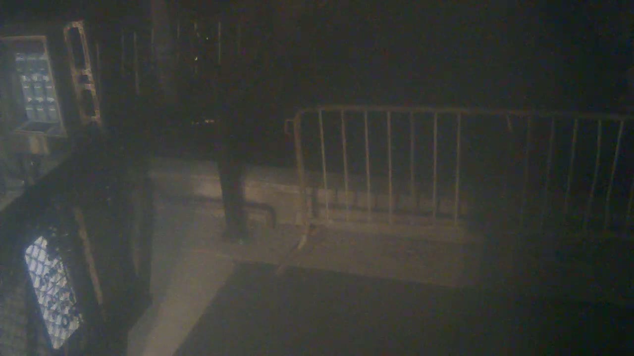 A dimly lit, dark area shows a metal barrier, a portion of a wall, and what appears to be part of a machine or structure.